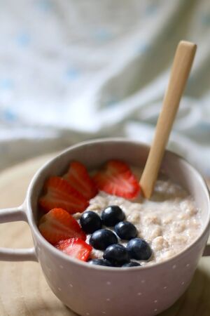 Bowl of vegan porridge with strawberry and blueberry topping, served in bed with floral sheets. Selective focus.の写真素材