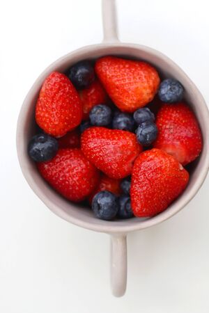 Ceramic bowl with fresh blueberries and strawberries. Top view, white background.の写真素材