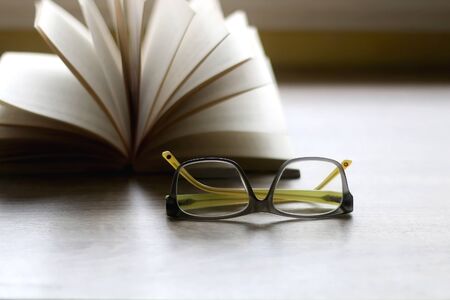 Reading glasses and open book on a table. Selective focus.