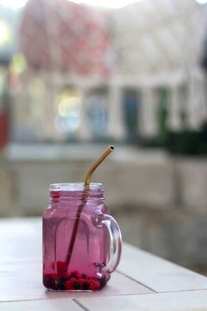 Cold water with frozen berries and reusable straw, served in a garden. Refreshing summer drink. Selective focus.の写真素材