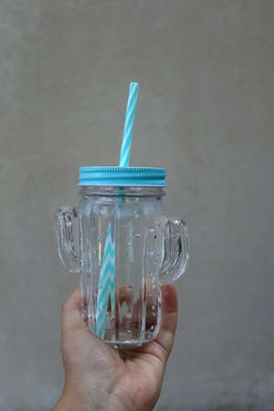 Hand holding cactus shaped bottle with cold water. Selective focus, gray background.の写真素材