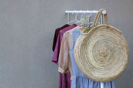Clothing rack with colorful floral dresses and wicker bag with flowers. Selective focus.の写真素材