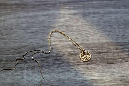 Gold necklace with vintage pendant, illuminated by sunlight. Selective focus, wooden background.の写真素材