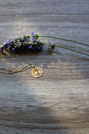 Gold necklace with vintage pendant and lavender flowers on wooden background. Selective focus.