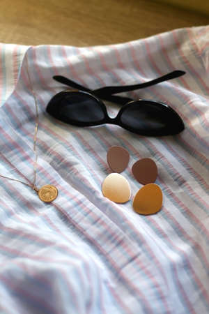 Striped pastel blouse, sunglasses, gold earrings and necklace. Selective focus.