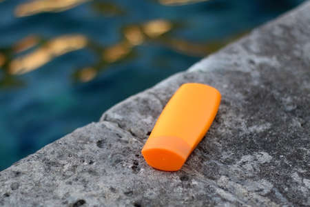 Bottle of sunscreen on a beach by the sea. Selective focus.