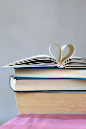 Stack of hardcover books. Top book has pages folded in a heart shape. Selective focus, grey background.の写真素材