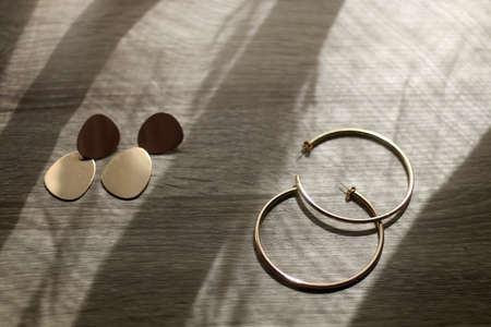 Golden statement earrings on wooden table, illuminated by sunlight. Selective focus.の写真素材