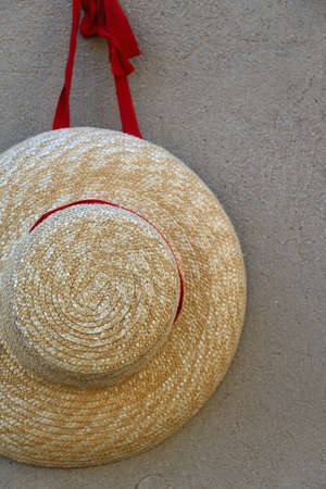 Straw hat with red ribbon, hanging on a concrete wall.の写真素材