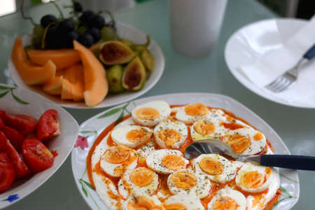 Boiled eggs with yoghurt sauce, tomato salda and various fruit on the breakfast table. Selective focus.の写真素材