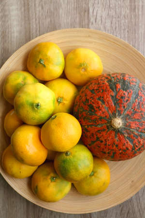 Bowl with tangeriens and pumpkin on wooden table. Top view.