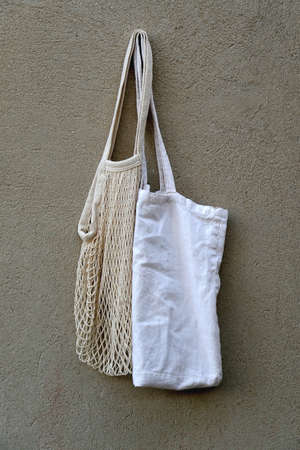 Cotton and mesh reusable bag hanging on a concrete wall.