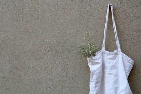 White reusable bag with gypsophila flowers, hanging on the wall.の写真素材