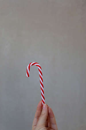 Unrecognizable person holding a candy cane decoration. Selective focus, simple background.