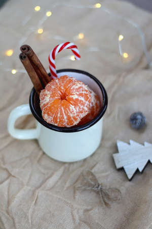 Mug with fresh tangerines, cinnamon sticks and candy cane. Christmas decorations on the table. Selective focus, bokeh lights.の写真素材