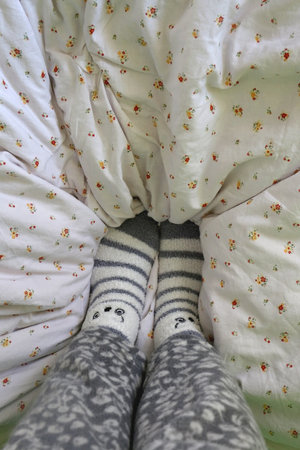 Feet in cute fuzzy socks on a bed. Top view, selective focus.の写真素材