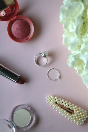 Silver rings, pearl barrette, various make up and flowers. Pastel background, top view.の写真素材