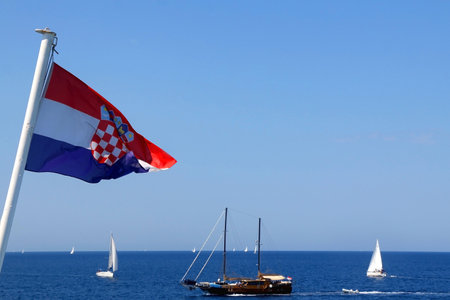 Flag of Croatia blowing in the wind. Adriatic sea and sailing boats in the background. Selective focus.の写真素材