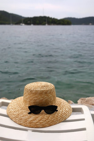Straw hat and cat eye sunglasses on the deck chair by the sea. Selective focus.