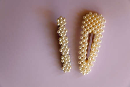 Two fashionable pearl barrette on pastel pink background. Top view.