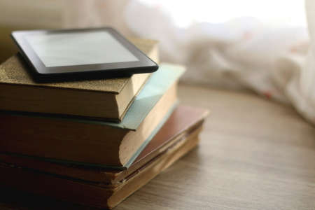 Stack of vintage books and e-book reader on top. Selective focus.