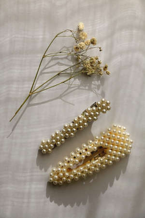 Two pearl hair clips and gypsophila flower on white background, illuminated by sunlight. Top view.の写真素材