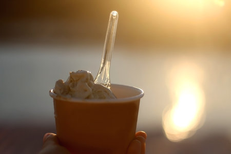 Hand holding a cup of ice cream at sunset. Selective focus.