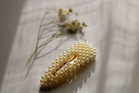 Pearl hair clip and gypsophila flower on white background, illuminated by sunlight. Selective focus.