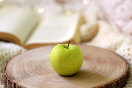 An apple, knitted blanket and open book on a bed. Cozy home details. Selective focus.