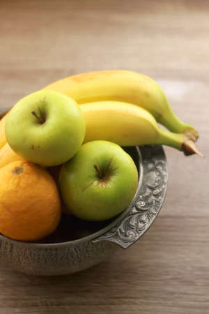 Antique bowl with bananas, apples and lemons on wooden table. Selective focus.の写真素材