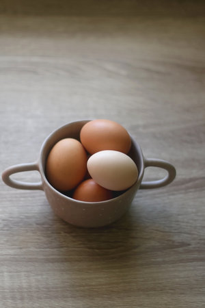 Ceramic bowl filled with fresh free range eggs on wooden table. Selective focus.