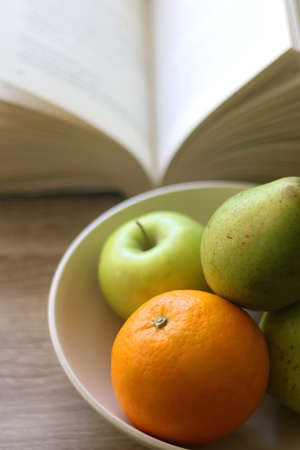 Bowl with pears, appples and oranges and open book on a table. Selective focus.の写真素材