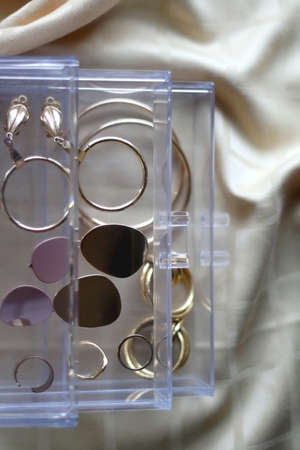 Transparent jewelry box filled with gold earrings and rings. Top view, selective focus.