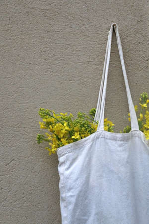 Linen bag filled with fresh yellow flowers, hanging on a concrete wall.