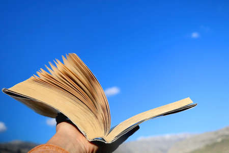 Hand holding open book up to the sky. Selective focus.の写真素材