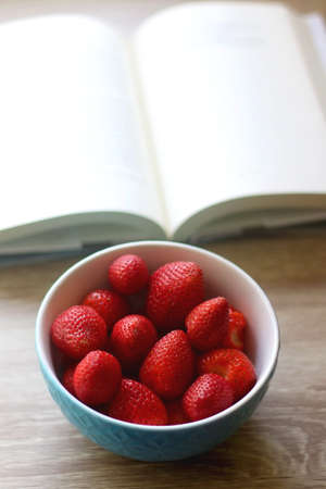 Bowl of fresh strawberries and open book on a table. Selective focus.の写真素材