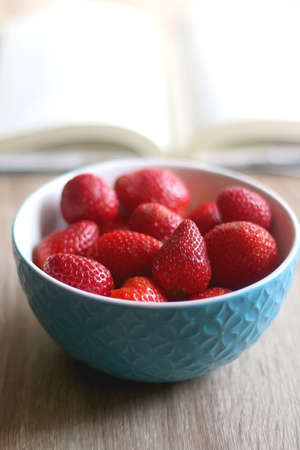Bowl of fresh strawberries and open book on a table. Selective focus.の写真素材