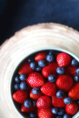 Bowl of blueberries and strawberries on wooden tray. Flat lay, dark textile background.の写真素材