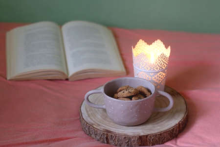 Bowl of chocolate chip cookies, lit candle and open book on a bed. Selective focus.の写真素材