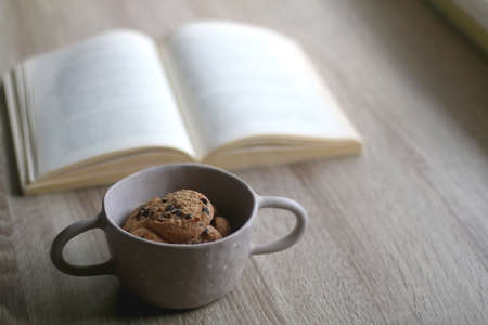 Bowl of chocolate chip cookies and open book on a table. Selective focus.の写真素材