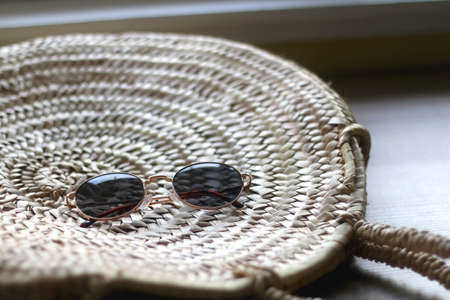 Wicker tote bag and round sunglasses on a table. Selective focus.の写真素材