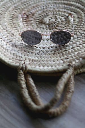 Wicker tote bag and round sunglasses on a table. Selective focus.の写真素材
