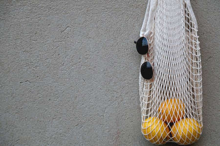 Reusable mesh bag filled with lemons and round sunglasses, hanging on the concrete wall.の写真素材