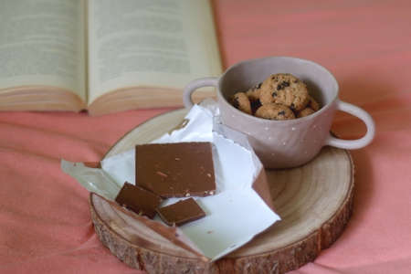 Chocolate bar, bowl of chocolate chip cookies and open book on a bed. Selective focus.の写真素材