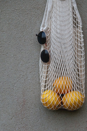 Reusable mesh bag filled with lemons and round sunglasses, hanging on the concrete wall.の写真素材