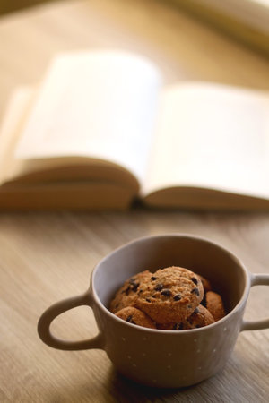 Bowl of chocolate chip cookies and open book on a table. Selective focus.の写真素材