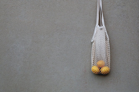 Reusable mesh bag filled with lemons, hanging on the concrete wall.