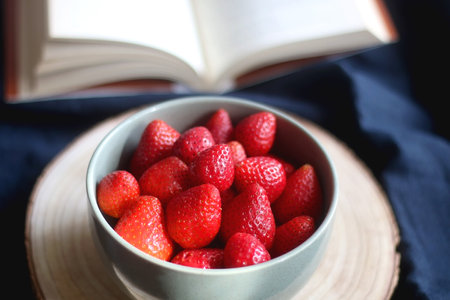 Bowl of fresh strawberries and open book. Selective focus, dark textile background.の写真素材