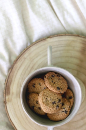 Bowl of chocolate chip cookies and wooden tray on a bed. Flat lay.