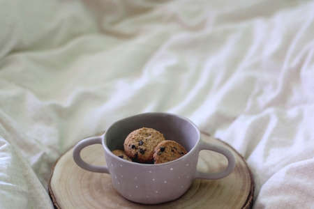 Bowl of chocolate chip cookies and wooden tray on a bed. Selective focus.